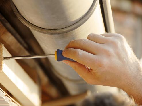 Hand mit Schraubendreher, der eine Schraube in ein Holzstück an einer hölzernen Unterkonstruktion einsetzt.